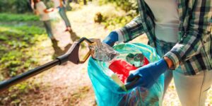 Eine Frau sammelt Müll auf und packt diesen in einen Müllsack und einige Kinder helfen ihr.